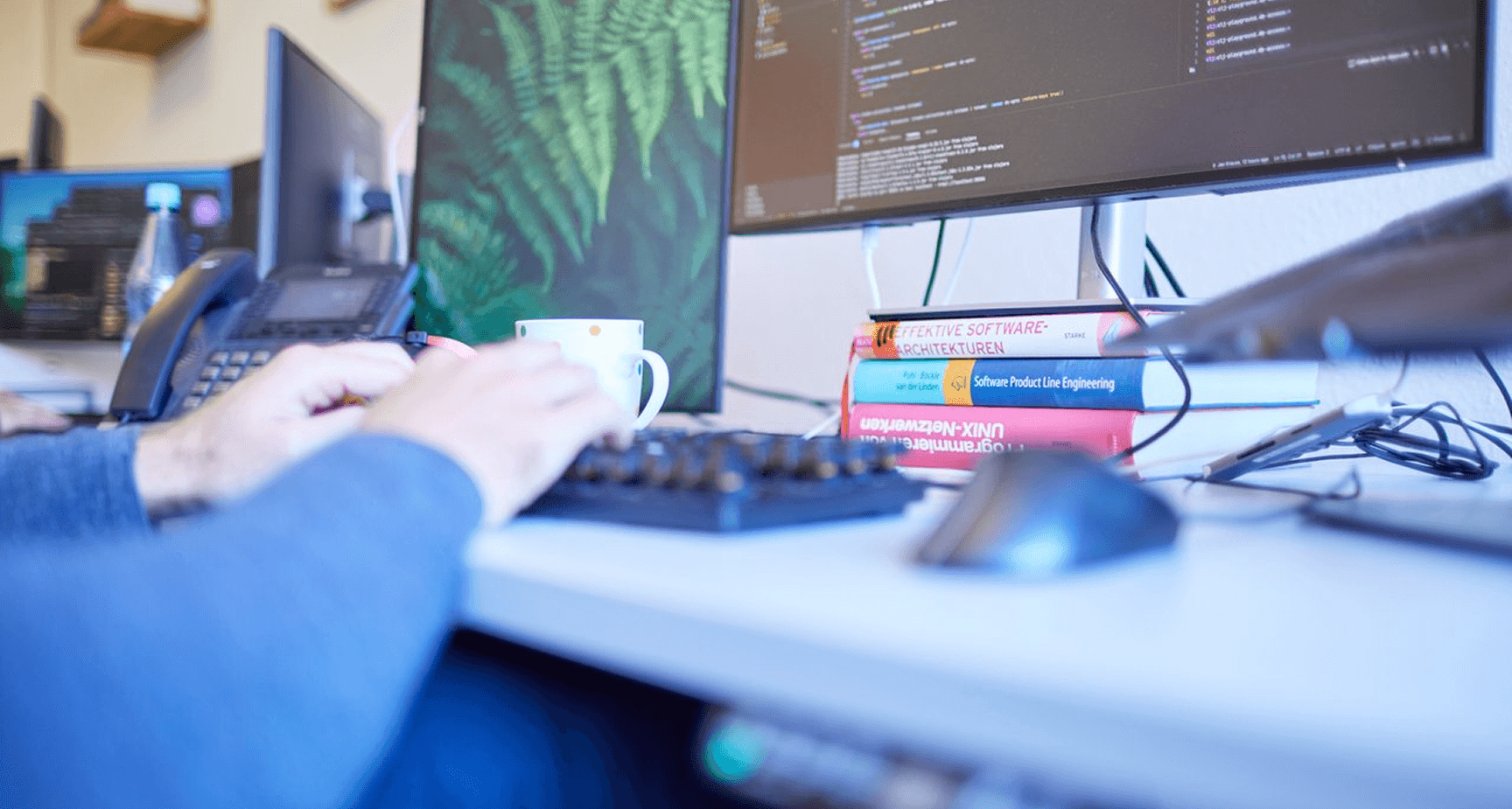 Arbeitsplatz mit Monitoren, Code-Editor und Fachbüchern zu Softwarearchitektur