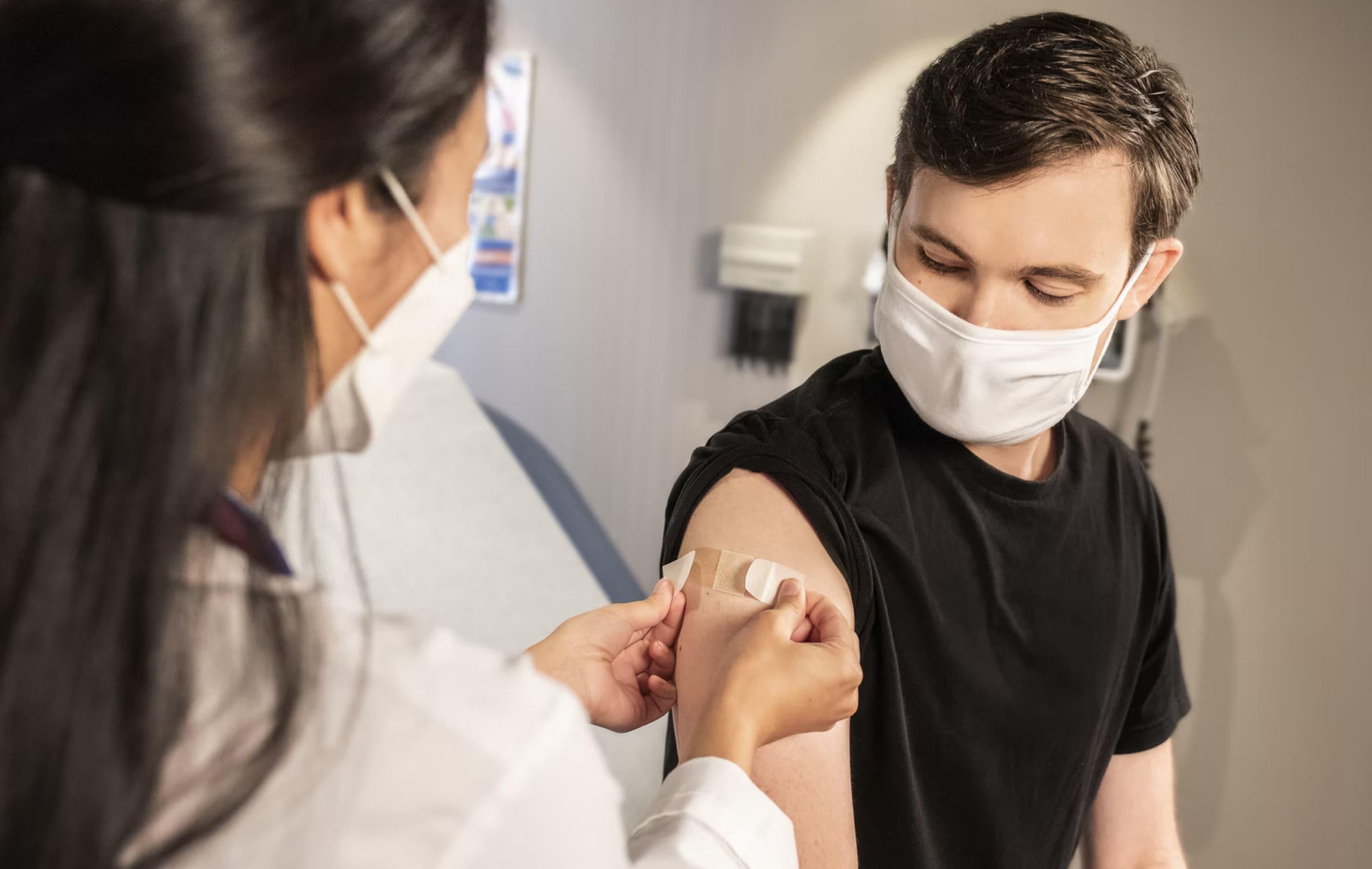 Eine medizinische Fachperson trägt ihrem Patienten nach der Impfung ein Pflaster auf.